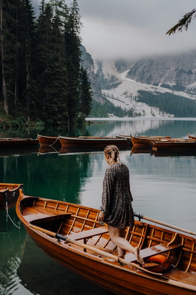 穿着黑白长袖衬衫的女人坐在湖边的棕色木船上